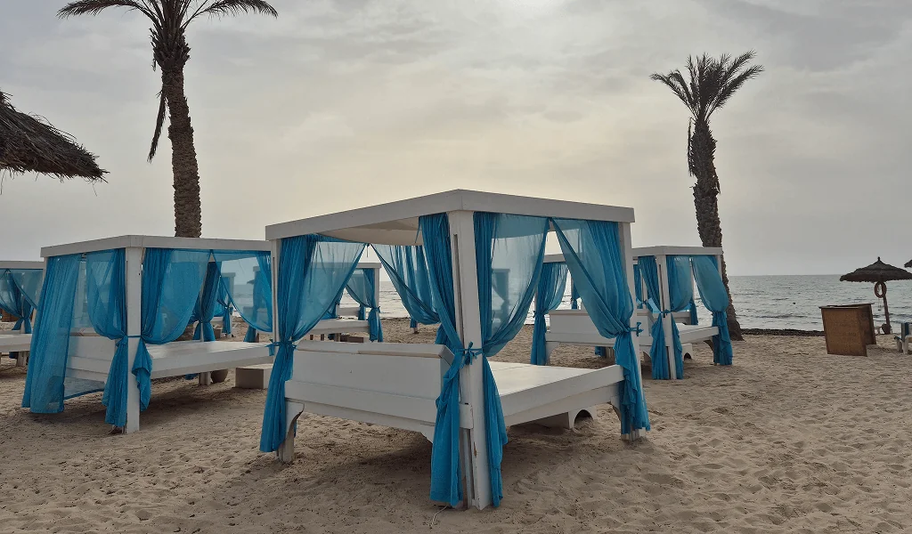 Weiße Strandbetten mit blauen Vorhängen am Strand von Djerba